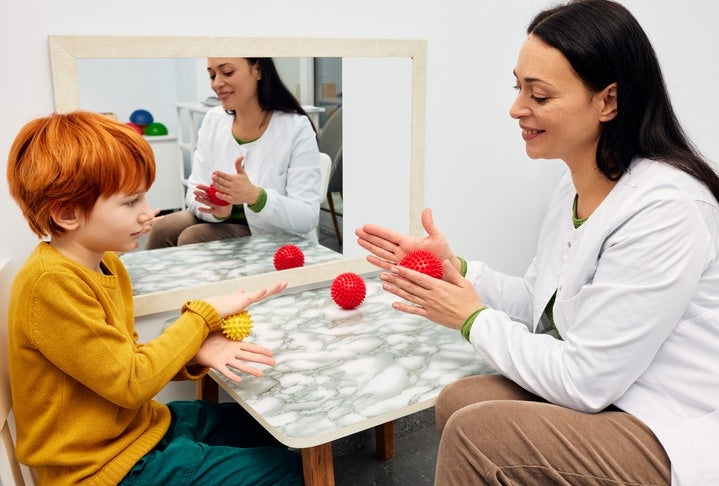 A therapist is helping a child with sensory therapy using toy balls in Houston, TX